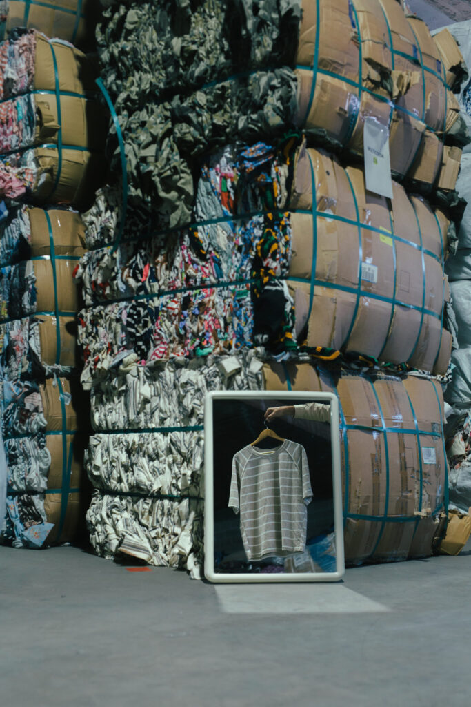 A striped recycled t-shirt reflected in a mirror in front of textile waste bales