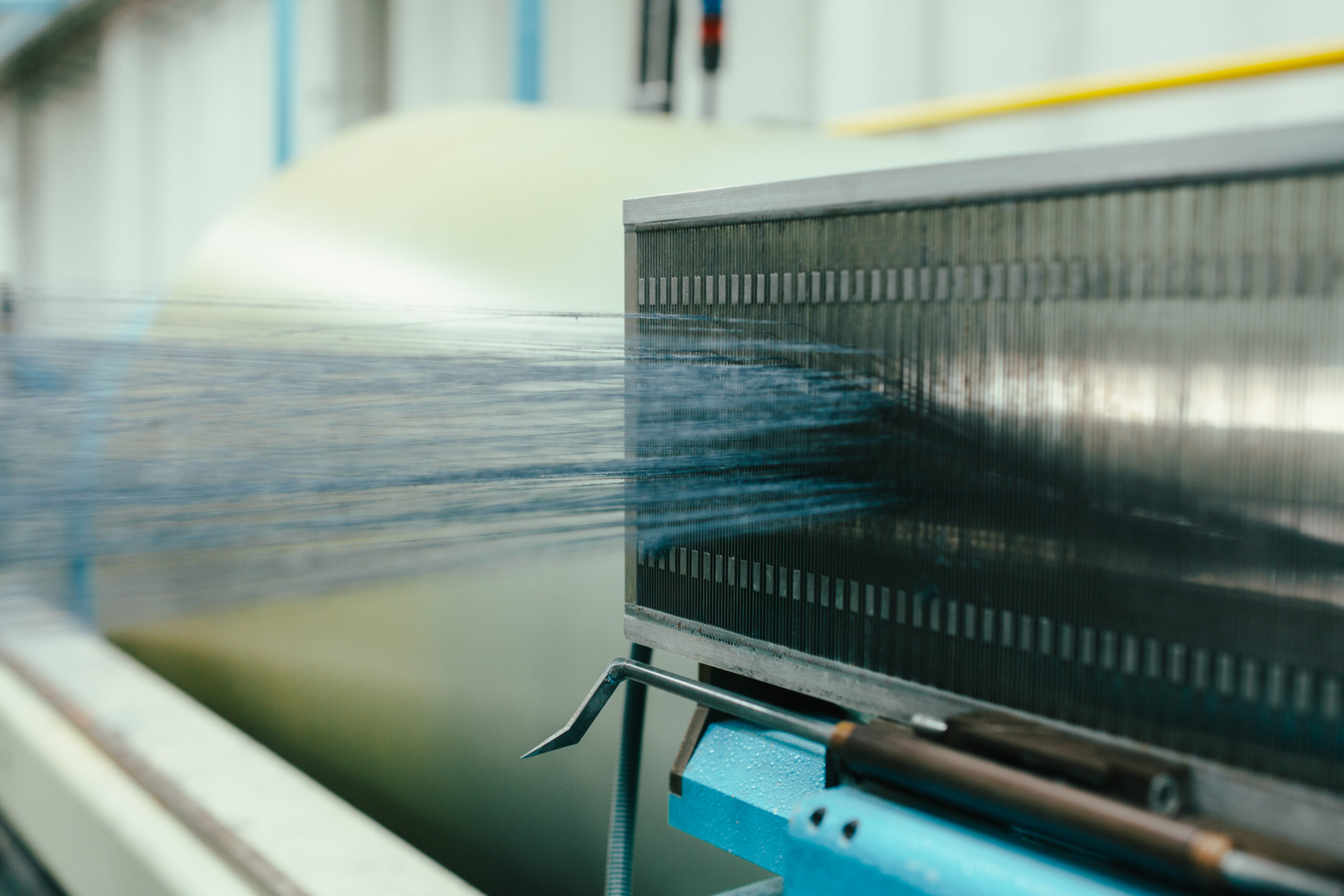 Blue yarn strands being woven through a loom in industrial textile production