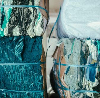 Fardos de residuos textiles en tonos verdes y azulados preparados para su reciclaje en planta de Coleo